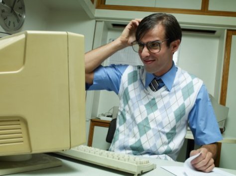 Man working at office desk, looking at computer and scratching head