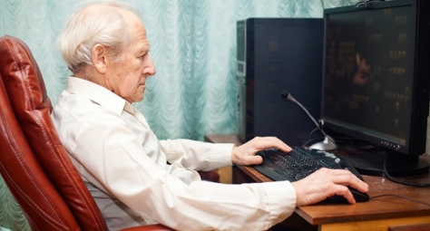old man sitting in a chair and working with computer